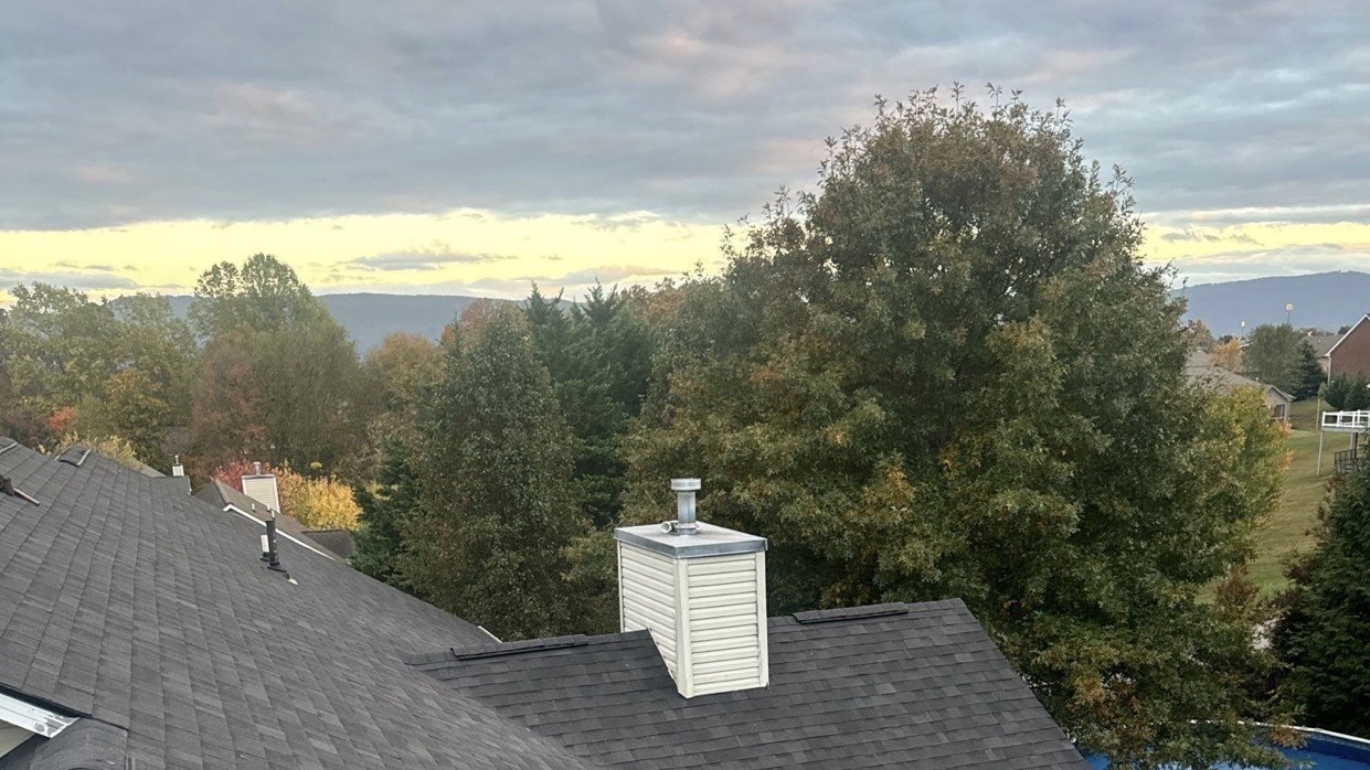 Dark architectural shingle roof and sided chimney at dusk, with autumn trees and the Smoky Mountain foothills behind