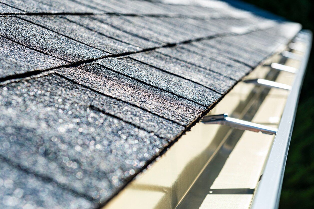 Close-up of an architectural shingle roof edge with a metal gutter and hidden hanger screw